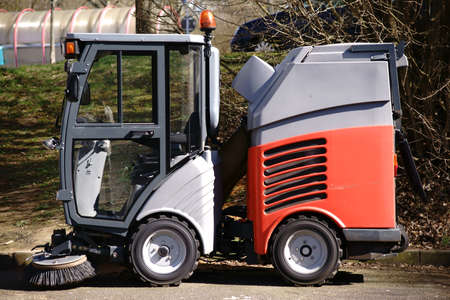 The side view of a small street cleaning vehicle with brush and a driver's cab with all-round...