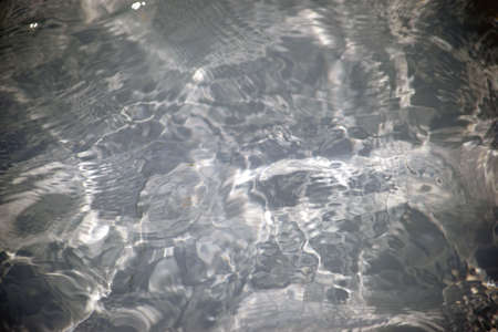 Whirl and wave patterns create abstract light reflections on the surface of the water.