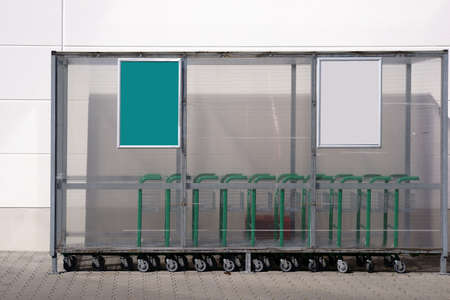 A plastic shelter with trolley outside in front of the entrance of a beverage dealer.