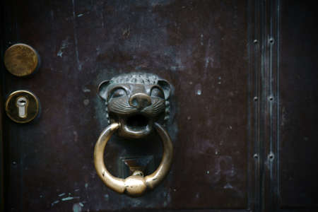 A worn metal doorknob shaped like a cat with a door knocker on a rusty church door.の写真素材
