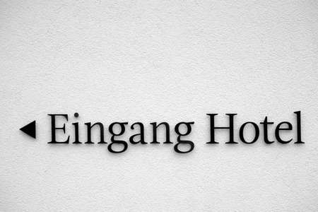 The entrance sign of a hotel on a white plaster facade with directional arrow.