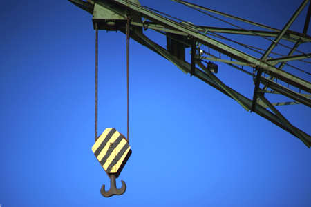 The massive crane hook of a lift crane in the harbor in front of a blue sky.