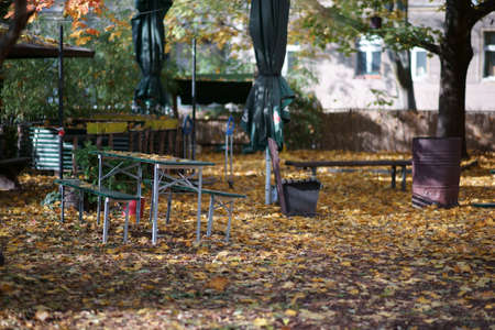 Benches and beer tables of a beer garden between falling leaves in autumn.