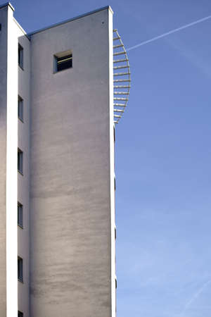 The massive exterior walls of a concrete industrial building with a spiral staircase on the corner.