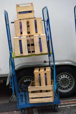 A trolley with empty wooden boxes is next to the truck of a dealer at the market.
