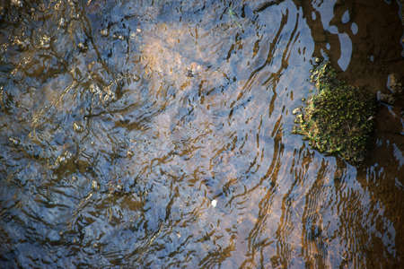 Whirl and wave pattern on a brook with stones under clear water.