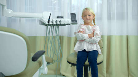 Little girl sit with hand on hand in dental chairの写真素材