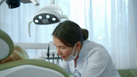 Dentist directs a lamp at the girls mouth and looks at her teeth.の写真素材