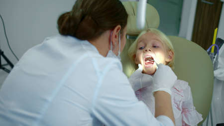 Female dentist directs a lamp at the girls mouth and looks at her teeth.の写真素材