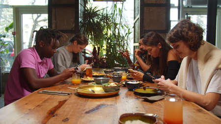 Multicultural friends sit in a cafe, they sit with phones in hands, girl laughの写真素材