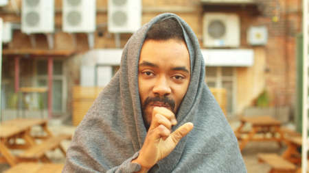 Man in grey blanket stand on the street and try to keep warmの写真素材