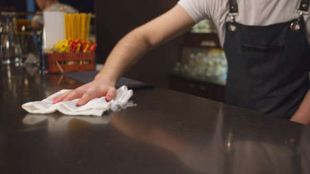 Bartender in the apron wipes bar counter with a rag, close up