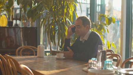 Adult man sit at a table in cafe and talk on phoneの写真素材