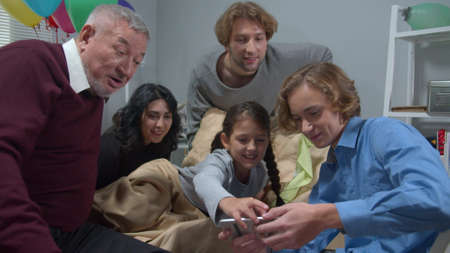 People visit girl in the hospital, boy show photo on phone and everyone laughの写真素材