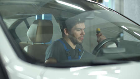 Mechanic with a tablet sits in a car and checks it