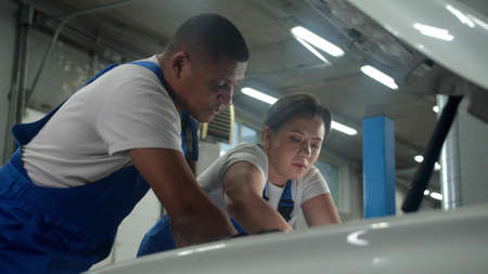 Mechanic holds a flashlight, woman in uniform repairs a car