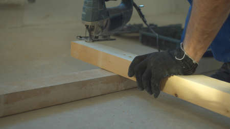 Repairman in uniform and gloves cuts off a piece of board