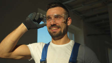 Smiling builder stands and puts off protective glasses, slow motionの写真素材