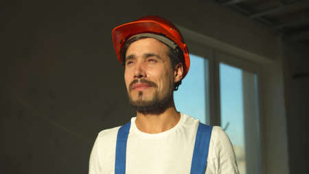 Slow motion, smiling builder stands and puts on protective helmetの写真素材