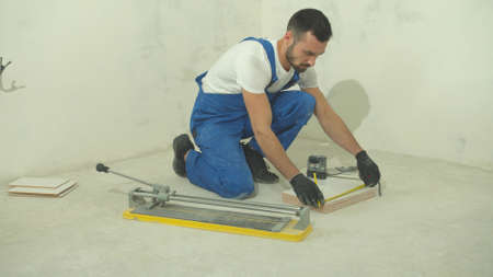 Builder in protective gloves measures a length of a tile