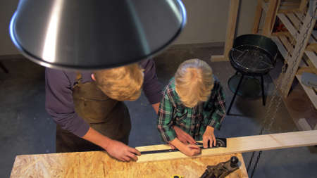 Man and little boy work with wood board in the workshop, slow motionの写真素材
