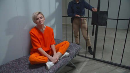 The criminal is sitting in the cell under the supervision of a guardの写真素材