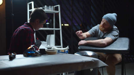 A man in a hat and beard communicates with a tattoo master in a tattoo parlorの写真素材