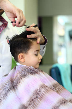 A lovely child in the hairdresser salon cutting his hairの写真素材
