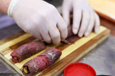 Chef hand preparing meat rolls on a wood cutterの写真素材