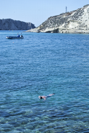 Man swimming in transparent water with boats and rocks on the backgroundの写真素材