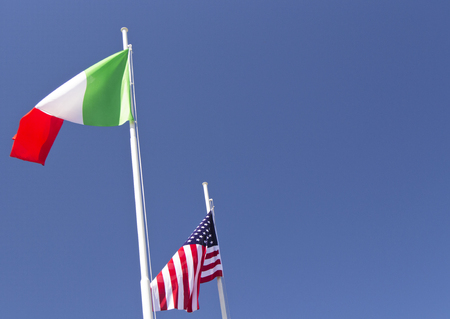 italian and usa flag waving in the wind with blue sky used as background.の写真素材