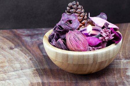 pourple tealight and dry potpourri in a wooden bowl over a table with black backgroundの写真素材
