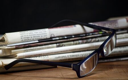 folded pile newspapers with a pair of blue reading glasses on it. free information and press concept