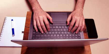 Caucasian male hands typing on a laptop pc keybord with mobile phone and squared block noted. Working conceptの写真素材