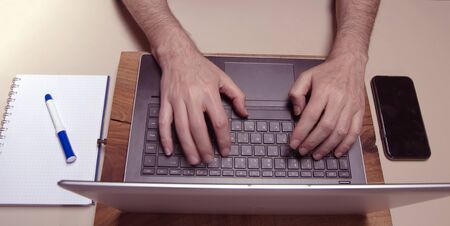Caucasian male hands typing on a laptop pc keybord with mobile phone and squared block noted. Working conceptの写真素材