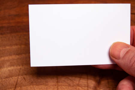 white empty card in male caucasian hand on a wooden background. concept for marketing and communicationの写真素材