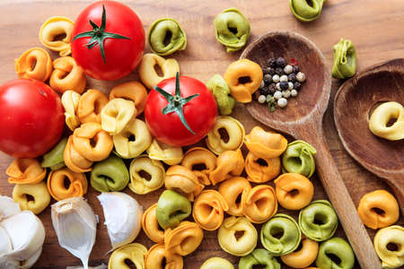 Raw tortellini pasta with tomatoes, garlic and wooden ladlesの写真素材