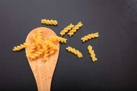 Fusilli pasta in a wooden ladle, black background