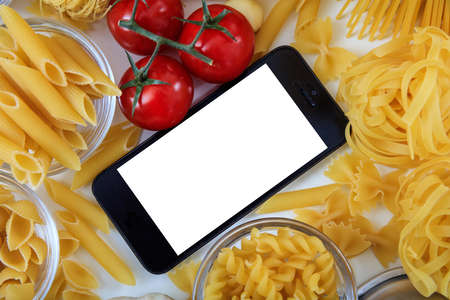 Smartphone with copy space on a white table with pasta and vegetablesの写真素材