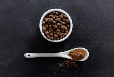 Allspice in porcelain bowl and spoon, black backgroundの写真素材