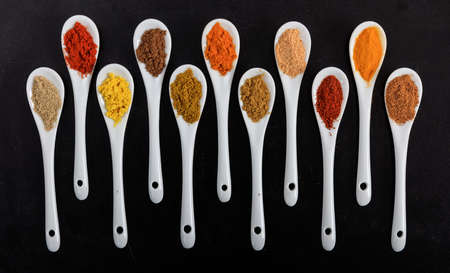 Various spices in porcelain spoons, black backgroundの写真素材