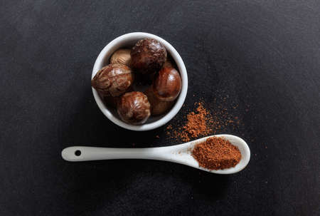 Nutmeg seeds and powder in porcelain bowl and spoon, black backgroundの写真素材