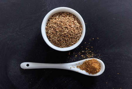 Cumin in porcelain bowl and spoon, black backgroundの写真素材