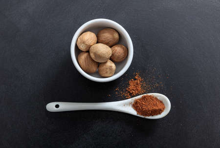 Nutmeg seeds and powder in porcelain bowl and spoon, black background