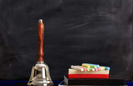 Colored chalks and a bell in front of a black chalkboardの写真素材
