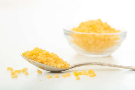 Yellow sugar in a spoon and a glass bowl on white backgroundの写真素材