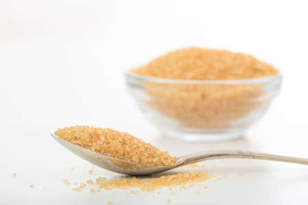 Yellow sugar in a spoon and a glass bowl on white backgroundの写真素材