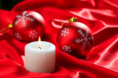 Red christmas balls and candle on red satin backgroundの写真素材