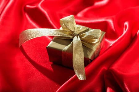 Golden gift box on a red satin backgroundの写真素材