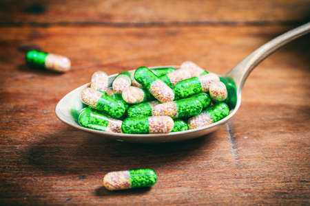 Colorful capsules in a spoon on a wooden background